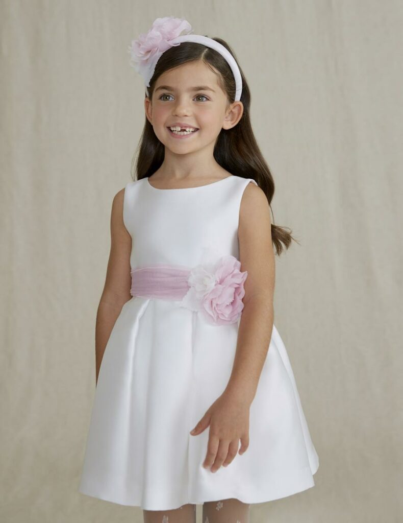 Fetiță într-o rochie albă elegantă cu floare roz și o bentiță albă cu floare roz