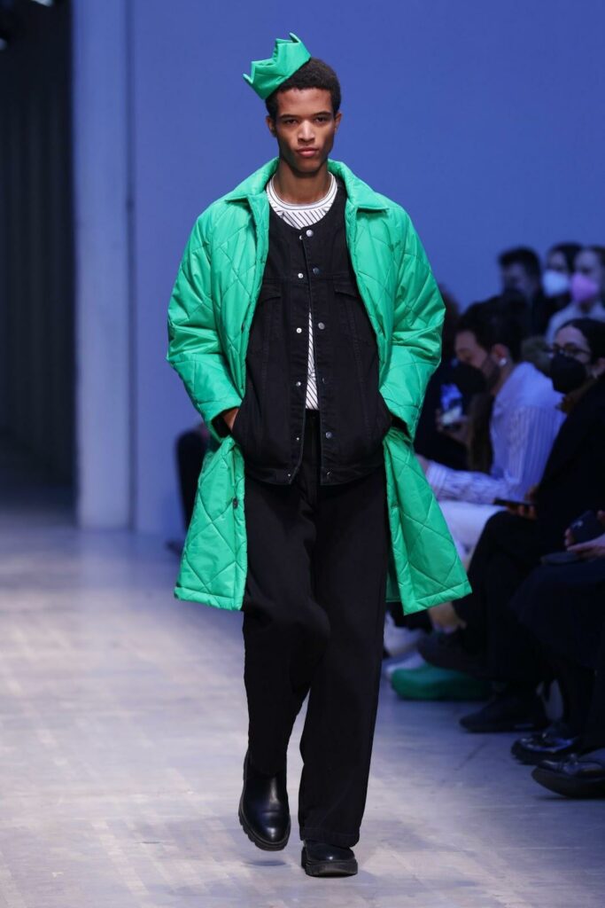 Model care poartă un palton verde matlasat, pantaloni, pantofi și top negru