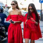 Două fete se plimbă pe stradă purtând rochii roșii și ochelari de soare