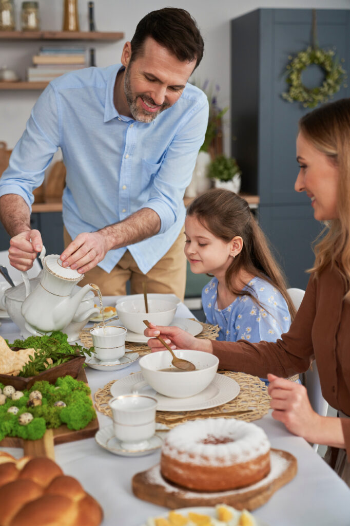 Familie la masa de Paște: un bărbat îmbrăcat într-o cămașă albastră toarnă ceai pentru o fată
