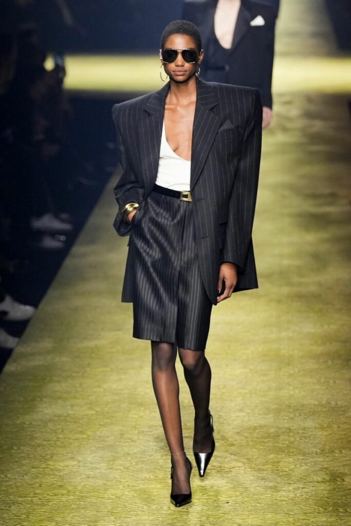 Un model pășește pe podium într-o fustă neagră și un sacou negru cu umeri oversize