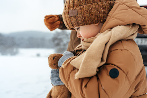 un băiat cu geacă, fular și căciulă maro într-un peisaj de iarnă
