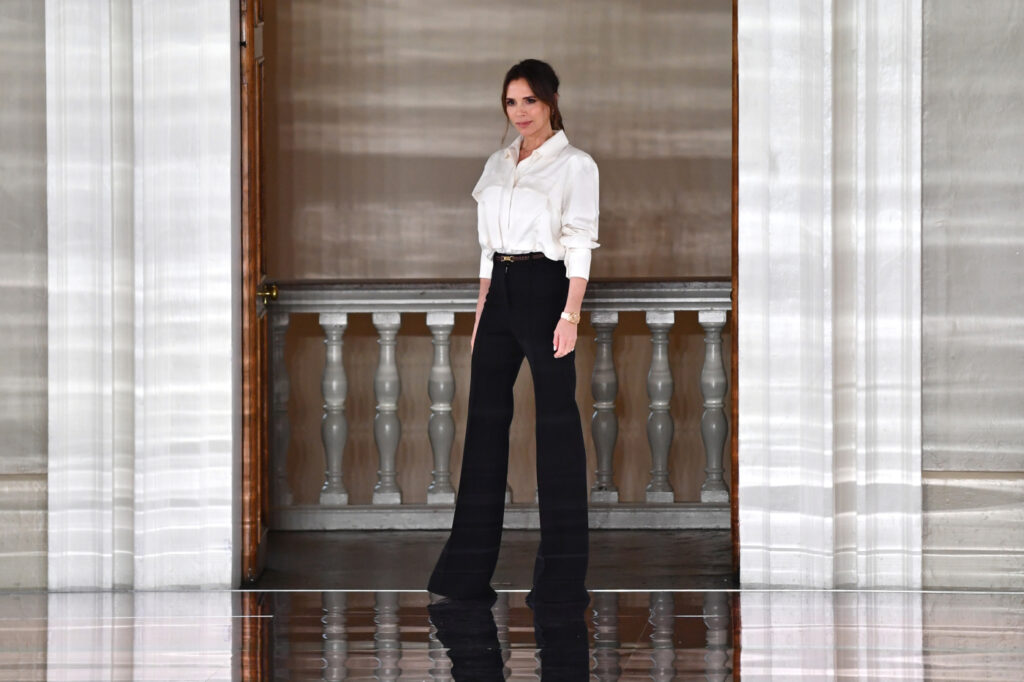 Victoria Beckham purtând o cămașă albă și pantaloni negri cu talie înaltă